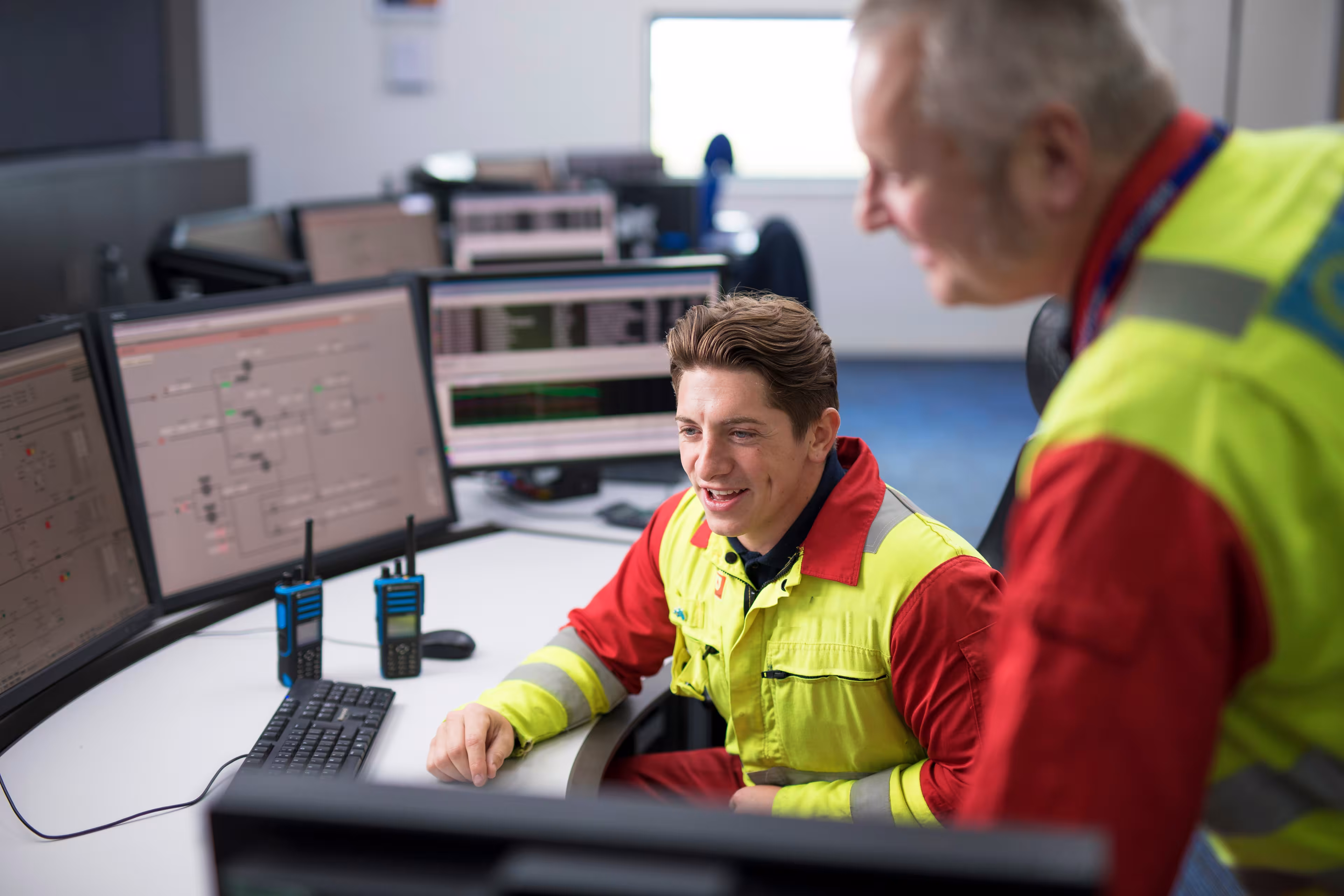 Two workers in high-visibility vests reviewing information on a computer monitor in an office setting